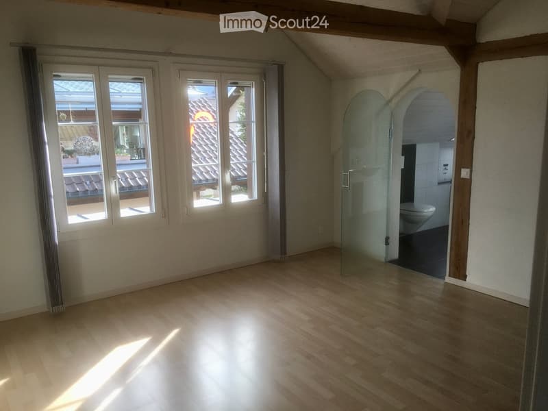 Empty room with wooden flooring, large windows, and a view of a tiled roof outside. A glass-enclosed shower area is visible in the background.