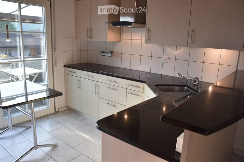 Modern kitchen with white cabinets, black countertops, a sink with a faucet, and a glass table near a large window.