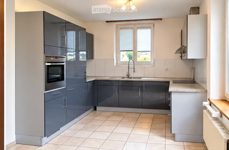 Modern kitchen with grey cabinets, stainless steel oven, sink, and countertop. Natural light from a window above the sink.