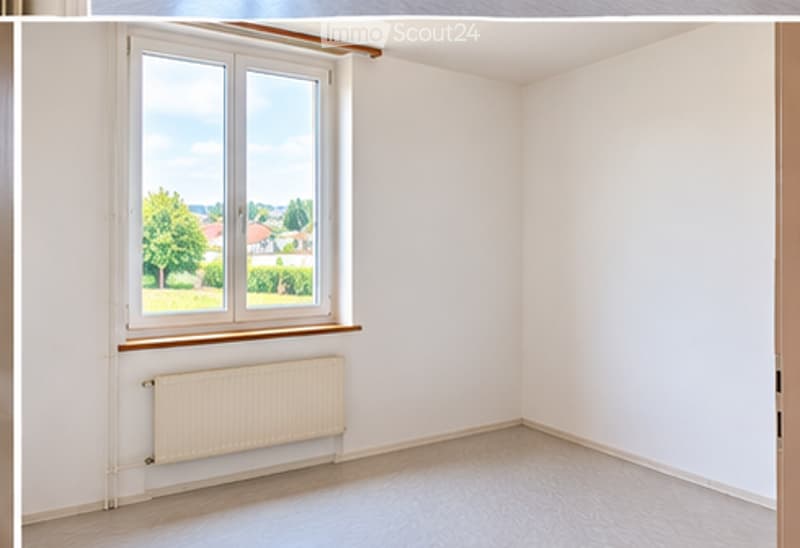Empty room with white walls, wooden flooring, a large window with a view of greenery, and a radiator below the window.