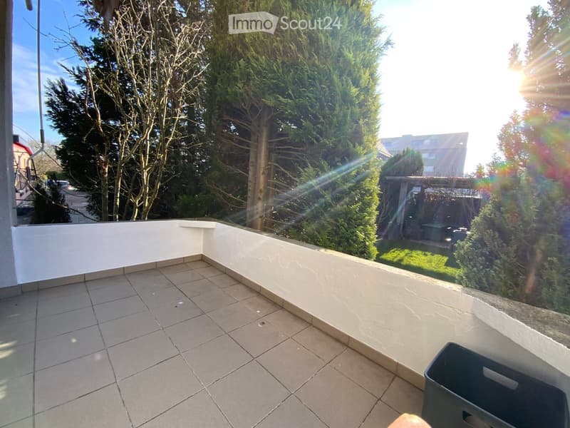 sunlit balcony with tiled floor, white walls, greenery and trees in the background