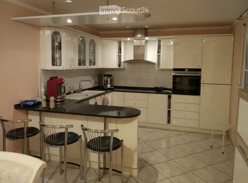 Modern kitchen with white cabinets, black countertop, stainless steel appliances, and three bar stools.