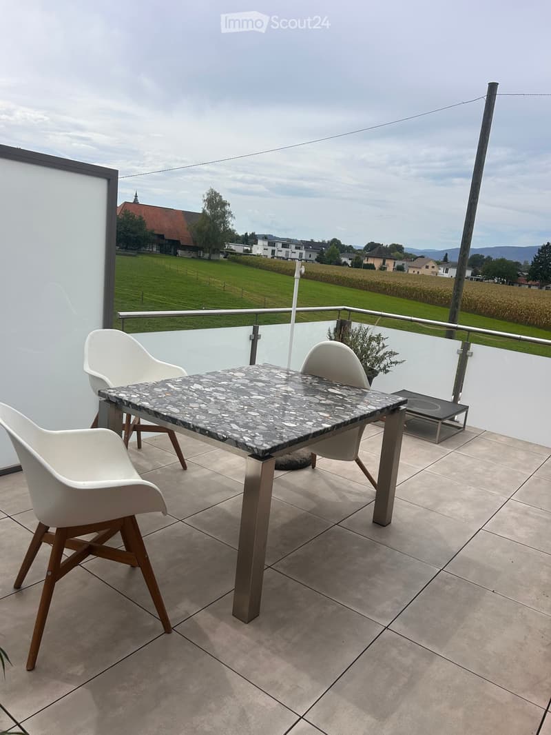 Balcony with a marble-top table, white chairs, and a view of a green field and houses.