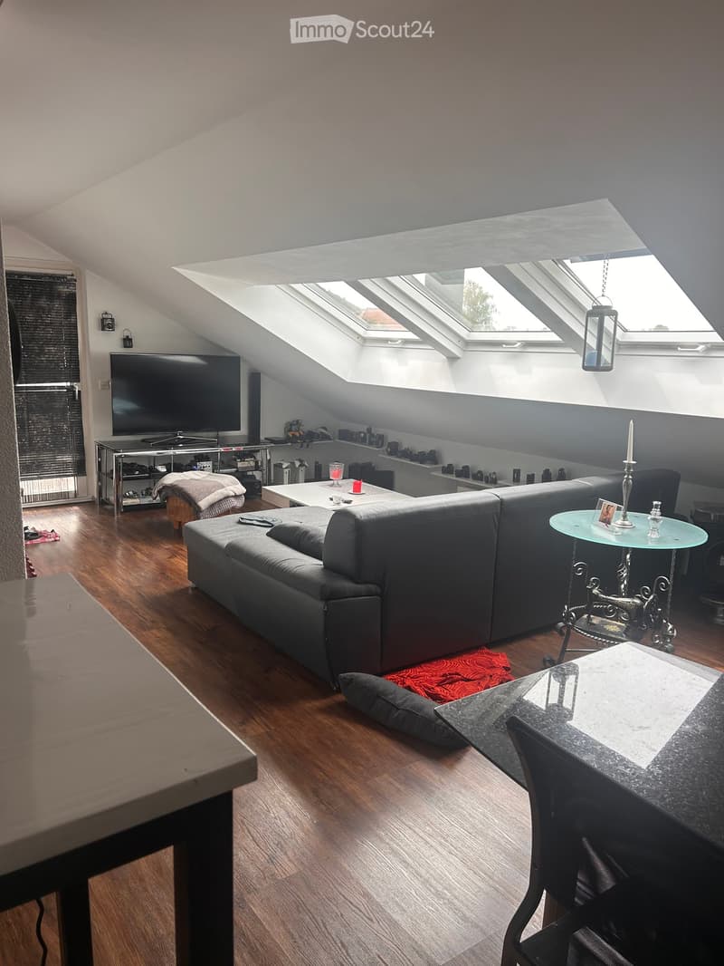 Modern living room with wooden flooring, grey sectional sofa, coffee table, TV, and decorative candle on a glass side table.