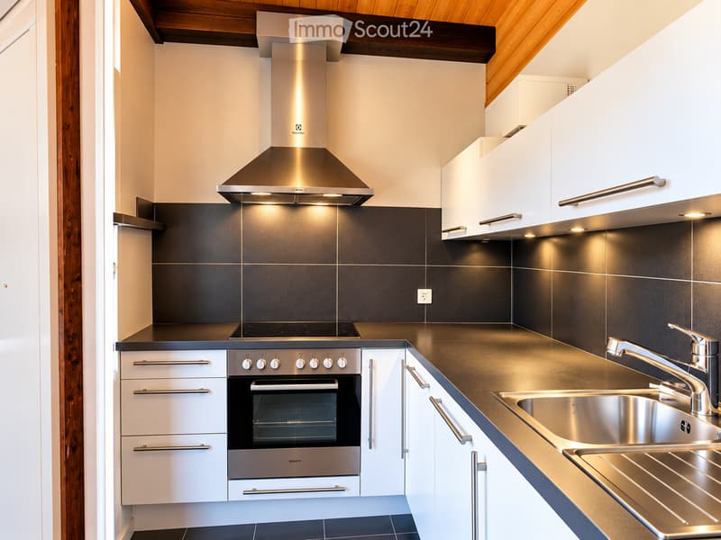 Modern kitchen with white cabinets, stainless steel appliances, dark countertops, and a sleek range hood.