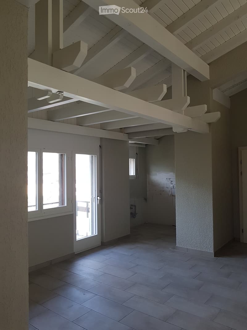 Empty room with exposed wooden beams on the ceiling, tiled floor, and large windows allowing natural light. No furniture or equipment is present.