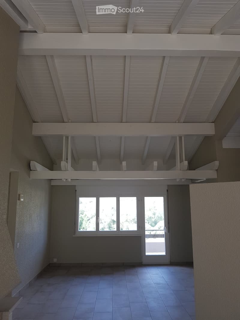 Empty room with tiled floor, large window, and white ceiling beams. No furniture or equipment visible.