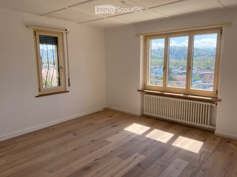 Empty room with wooden flooring, white walls, and two windows offering a view of the outside. No furniture or equipment is present.