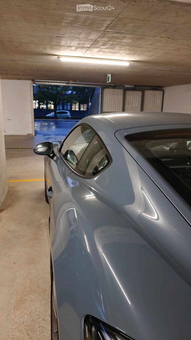 Underground parking area with a silver car parked inside, concrete floors and walls, and a visible exit to the outside.
