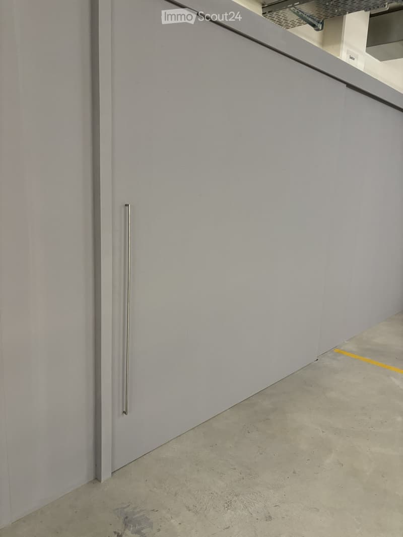 Empty room with white walls, grey floor, and a closed white cabinet with a silver handle.