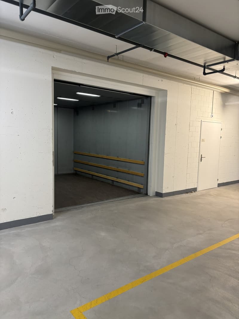 Empty underground parking area with concrete floors, white brick walls, and a large open garage entrance.