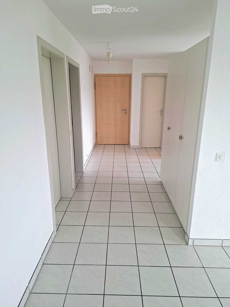 Empty hallway with tiled floor and white walls, featuring several doors and a light fixture on the ceiling.