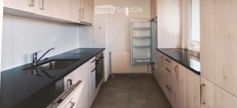 Modern kitchen with white cabinets, black countertops, stainless steel sink and faucet, built-in oven, and refrigerator.