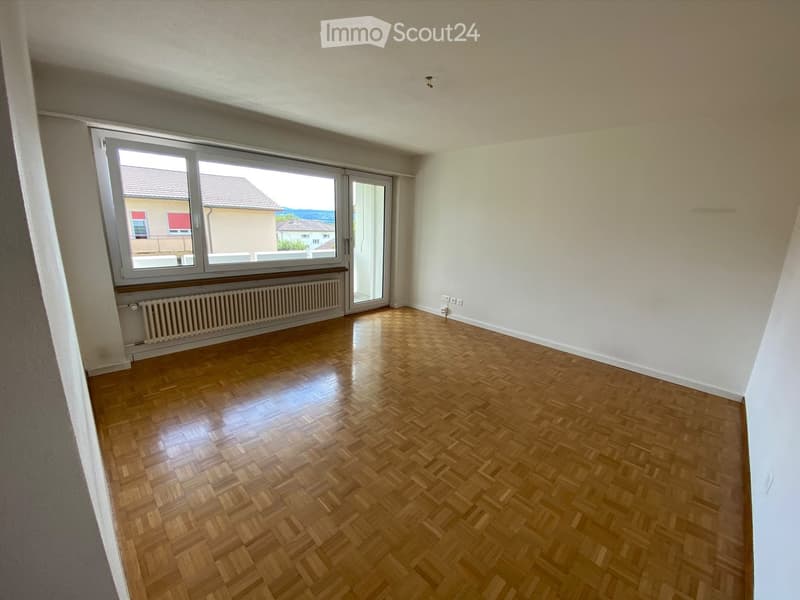 Empty room with wooden parquet flooring, white walls, large window with sliding glass door, radiator, and visible electrical outlets.