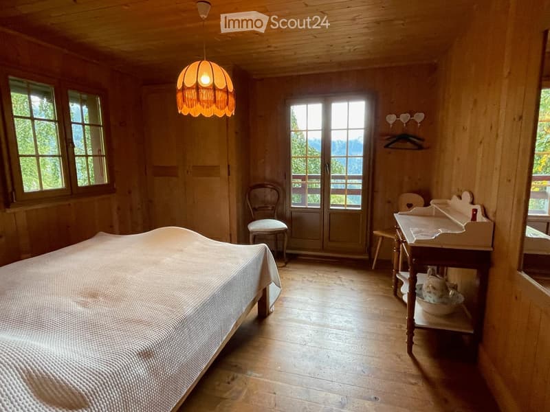 Cozy wooden bedroom with a large bed, wooden floor, large windows, and a view of the mountains.