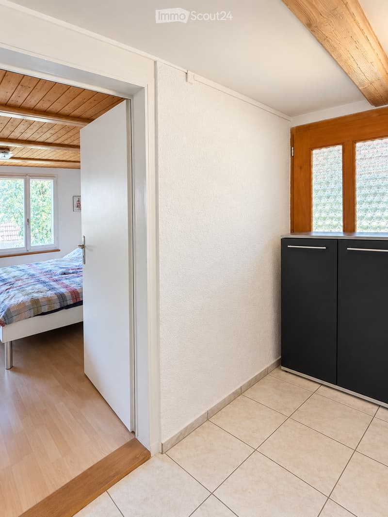A small, modern room with a bed and a cabinet, featuring wooden flooring and white walls.