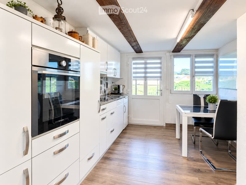 Modern kitchen with white cabinets, stainless steel oven, wooden flooring, and a small dining area with a table and chairs.