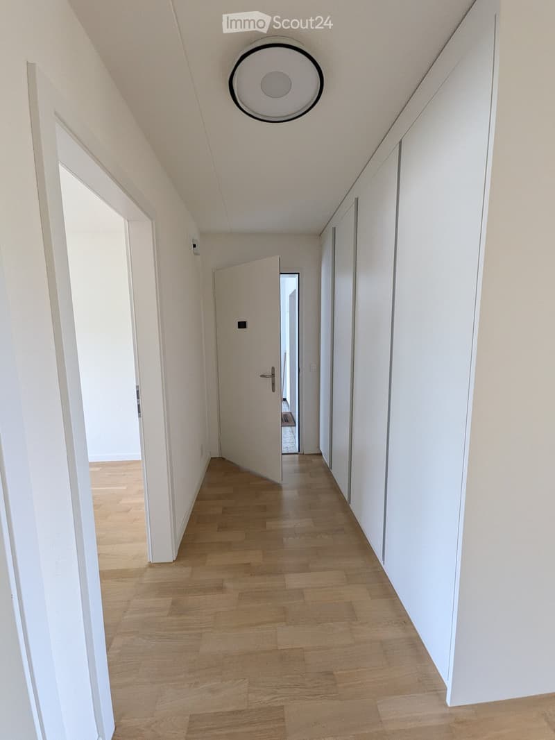 A clean, modern hallway with light wooden flooring, white walls, and several doors leading to other rooms.