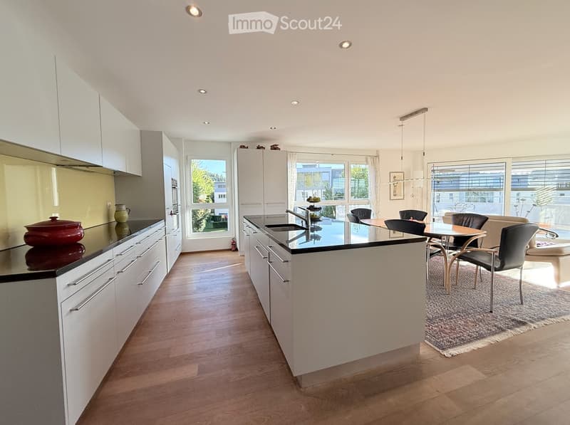 Modern kitchen with white cabinets, black countertops, and a central island. The space features a dining area with a table and chairs, a sink, and various kitchen appliances.