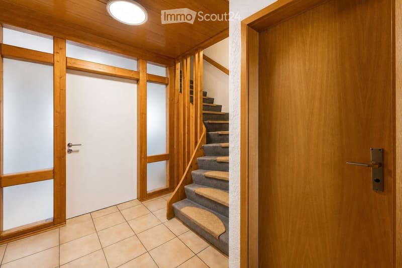 Hallway with wooden walls, tiled floor, and a staircase leading upwards with carpeted steps and wooden railings.