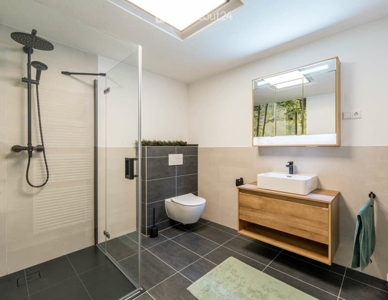 Modern bathroom with a glass-enclosed shower, a toilet, a sink with a wooden cabinet, a large mirror, and a towel on a rack.