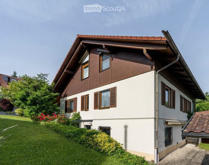 Two-story house with a combination of wooden and white exterior walls, multiple windows with shutters, and a well-maintained garden with green lawns and colorful flowers.