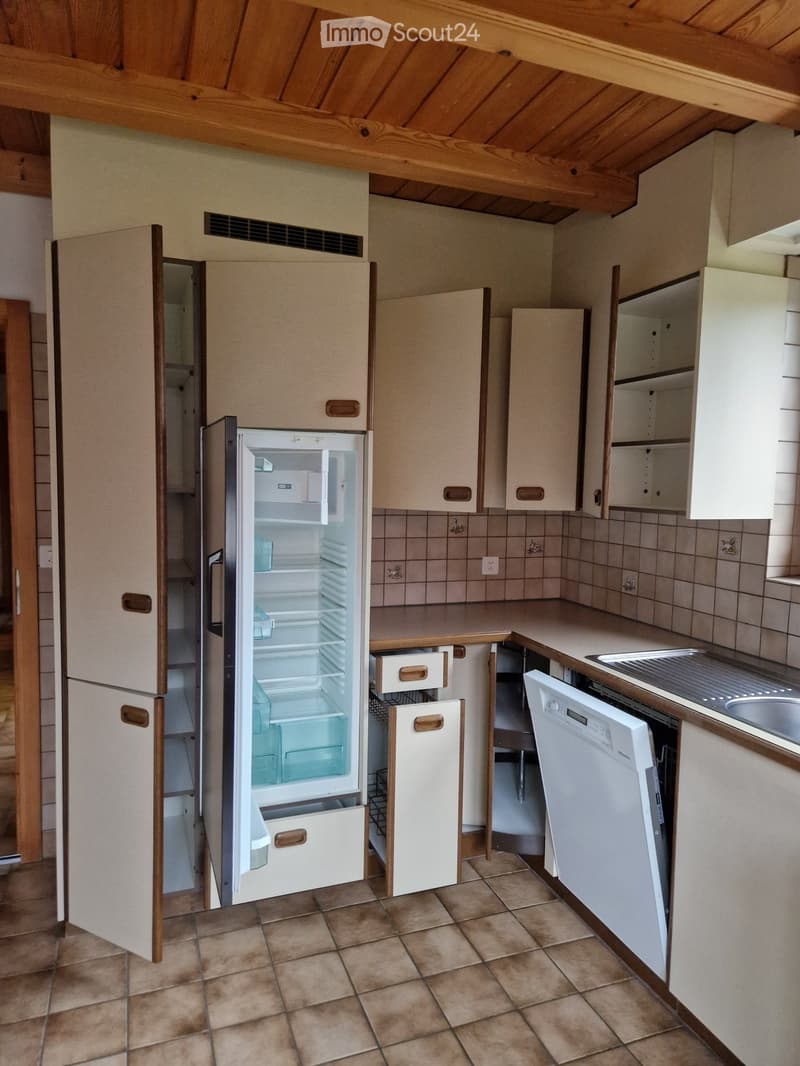 A modern kitchen with light-colored cabinets, a refrigerator, dishwasher, and a sink, featuring tiled walls and a tiled floor.
