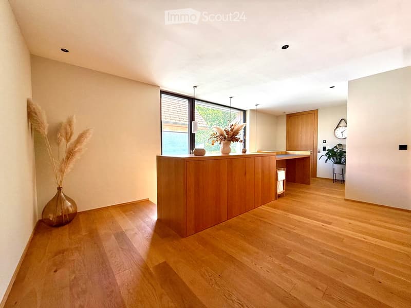 Bright, minimalist hallway with wooden flooring, a wooden counter, a vase with dried plants, a clock on the wall, and a small plant on a stand.