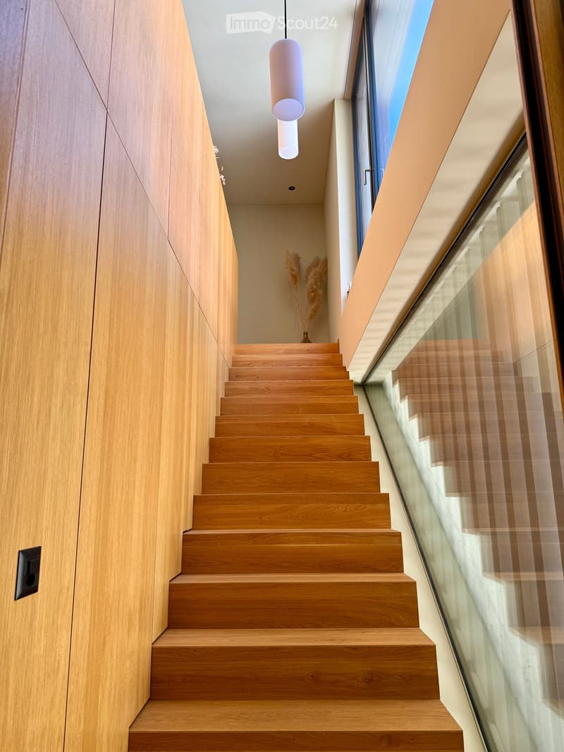 Modern wooden staircase with glass railing, pendant light fixture, and neutral-toned walls.