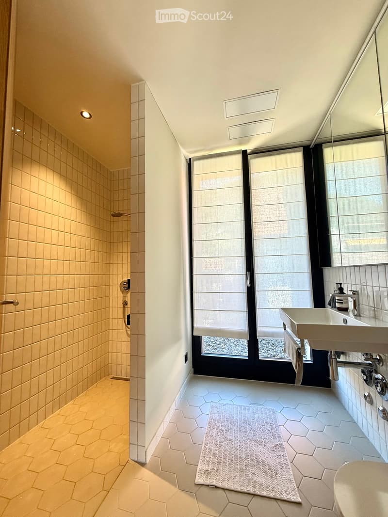 Modern bathroom with hexagonal tiles, a large window with blinds, a sink with a modern faucet, a bathtub, and a shower area with a glass enclosure.