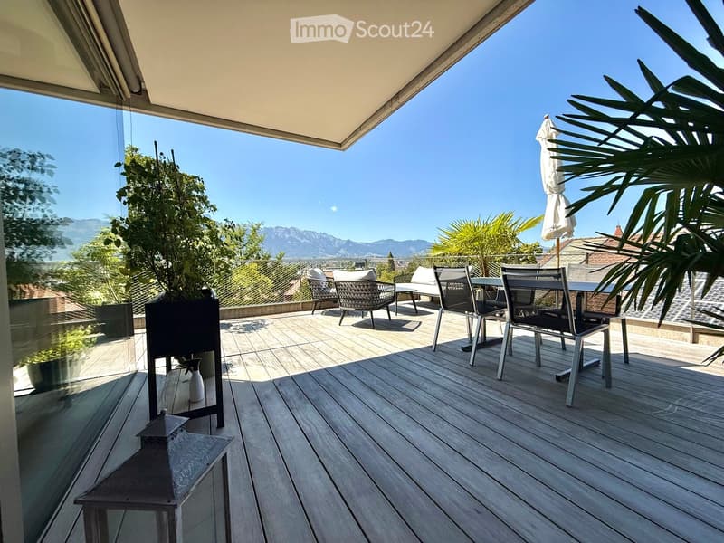Wooden deck with outdoor furniture, including a table, chairs, and an umbrella, overlooking a scenic mountain view.