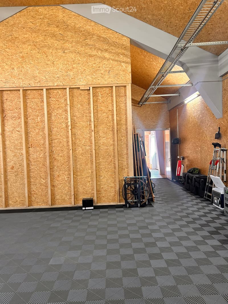 Empty room with exposed wooden walls, grey patterned floor, and a ladder leading to an attic space.