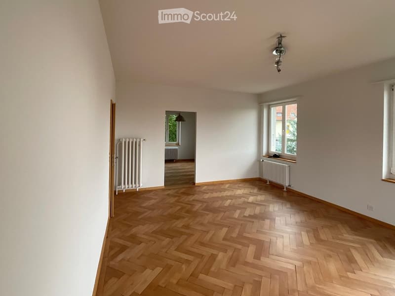 Empty room with wooden herringbone flooring, white walls, radiators, and large windows. No furniture or equipment present.