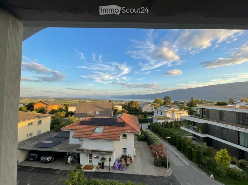 Balcony view overlooking a residential area with houses, solar panels, parked cars, and distant mountains.