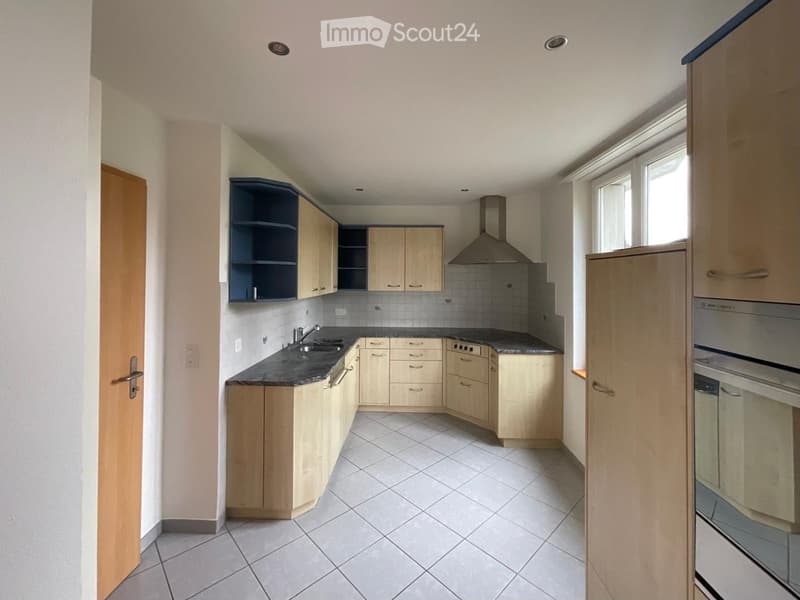 Modern kitchen with light wooden cabinets, stainless steel appliances, and a black countertop.