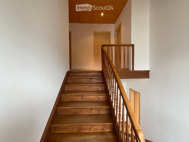 Wooden staircase with a wooden handrail and balusters, leading to an upper level with a landing and doors.