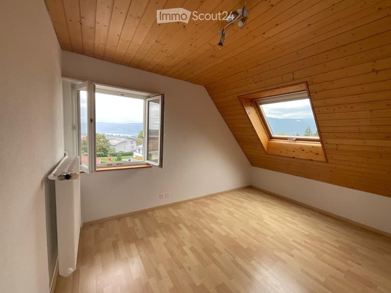 Empty attic room with wooden floors, wooden slanted ceilings, and large windows offering a scenic view.