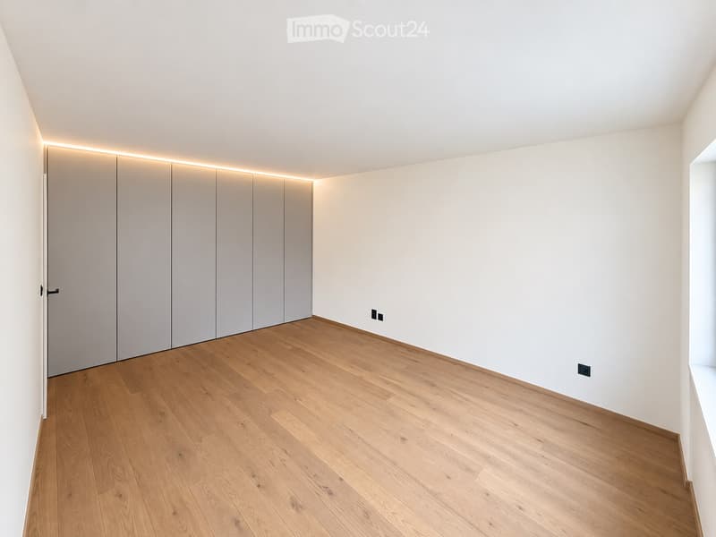 Empty room with light wooden flooring, white walls, and built-in closet with sliding doors.