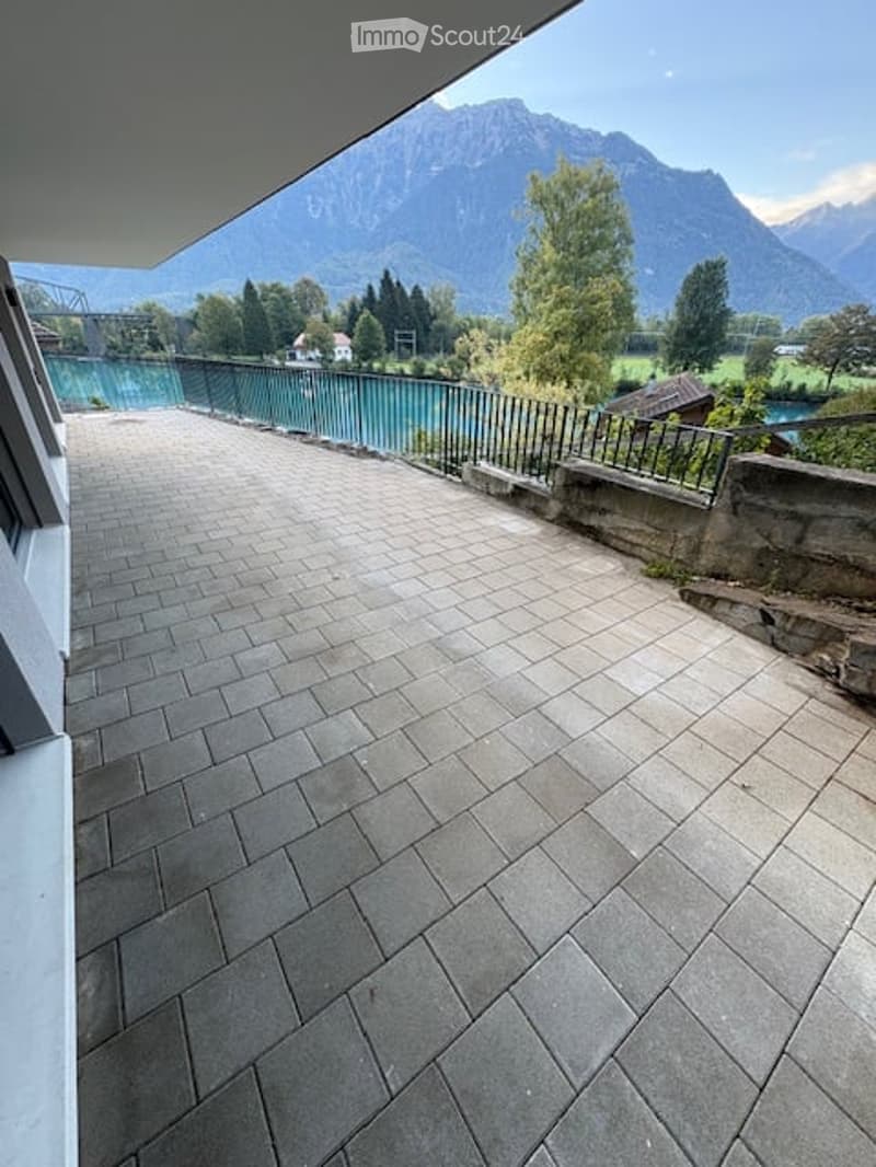 Balcony with stone tiles, metal railing, overlooking a river and mountain landscape.