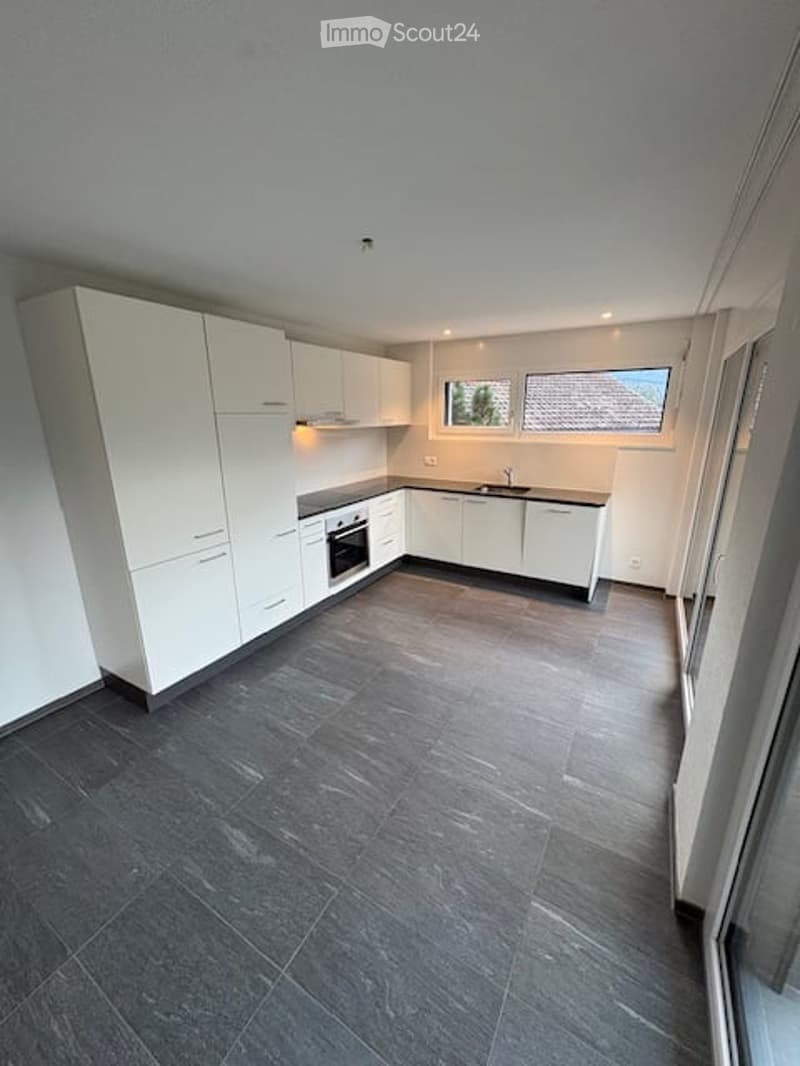 Modern kitchen with white cabinets, dark tiled floor, and built-in appliances including an oven and sink.