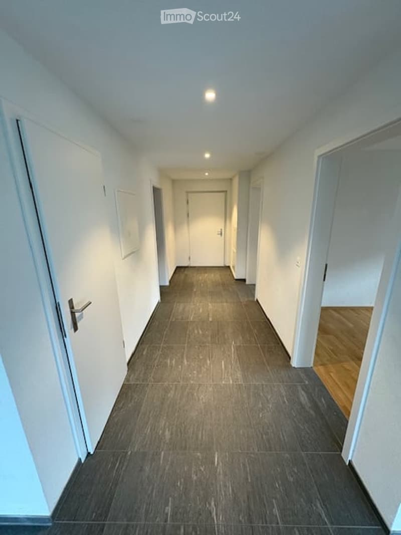Empty hallway with dark grey tiled floor, white walls, and several doors on both sides.