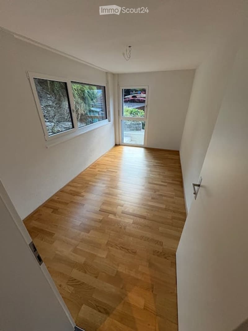 Empty room with wooden flooring, white walls, large windows, and a door leading outside.
