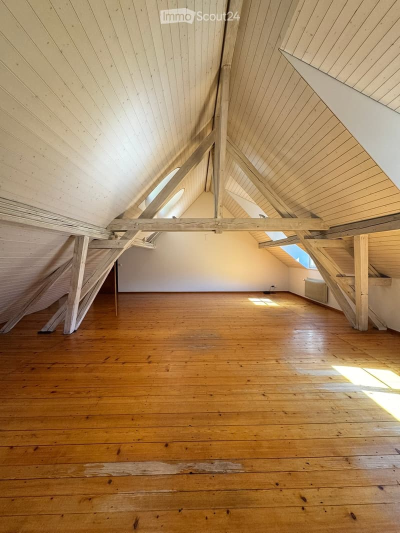 Empty attic space with wooden floors, exposed wooden beams, and skylights allowing natural light to enter.