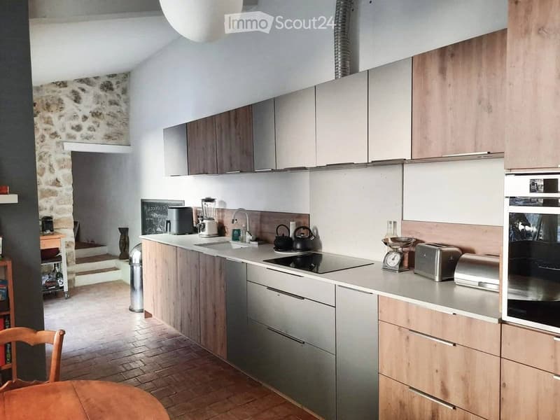 Modern kitchen with wooden cabinets, stainless steel countertops, induction stove, sink, oven, toaster, trash bin, chandelier