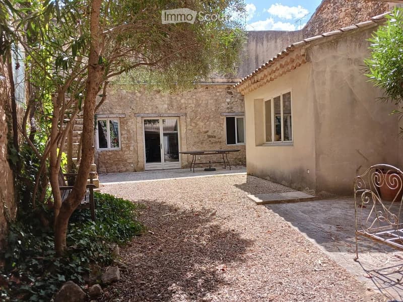 Courtyard with stone building, paved courtyard, stairs, wooden bench, plants, and small table.
