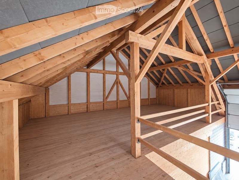 An empty room with exposed wooden beams and a wooden floor, featuring a large open space and a small balcony area with wooden railings.