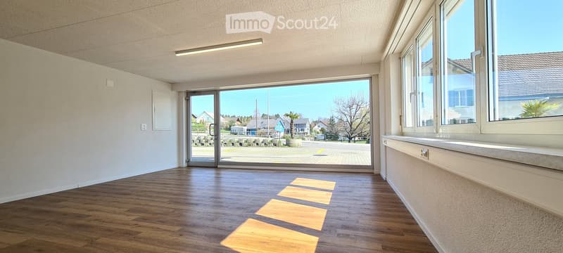 Empty room with wooden flooring, large windows, and a sliding glass door leading outside.