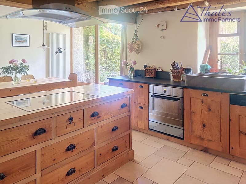 Bright kitchen with wooden island, induction cooktop, oven, sink, and cabinets. Features a vase with flowers and a hanging light fixture.