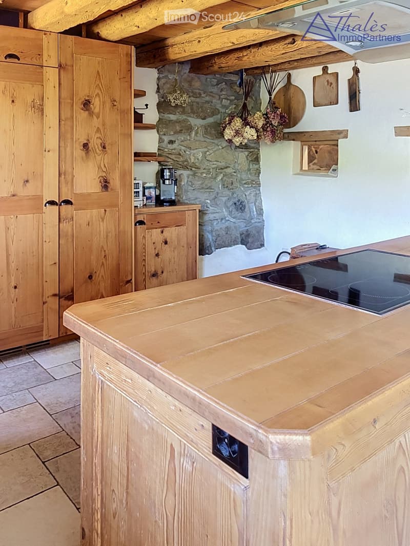 A rustic kitchen with wooden cabinets, a wooden countertop, and an electric stove. The back wall features a stone accent and wooden shelves holding decorative items and a coffee maker.