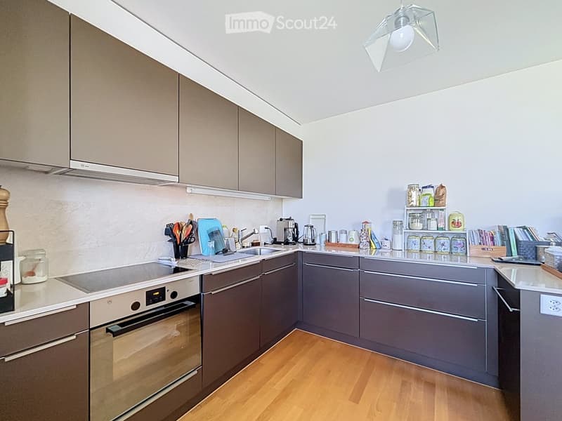 Modern kitchen with grey cabinets, stainless steel appliances, wooden flooring, and various kitchen items on the counter.